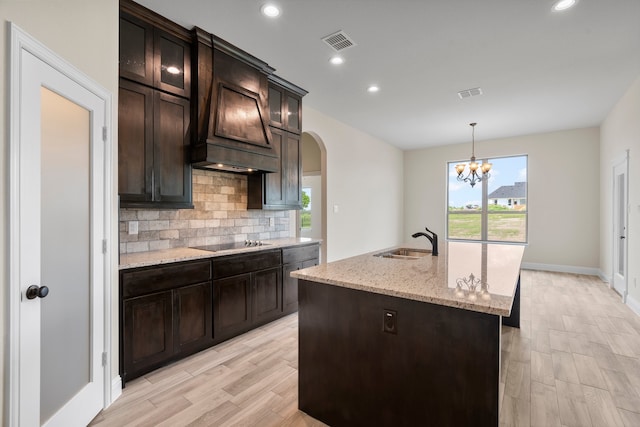 kitchen with black electric stovetop, hanging light fixtures, sink, dark brown cabinets, and a center island with sink