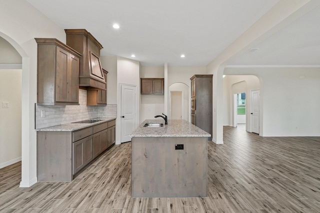 kitchen featuring sink, light stone counters, a kitchen island with sink, and black electric cooktop