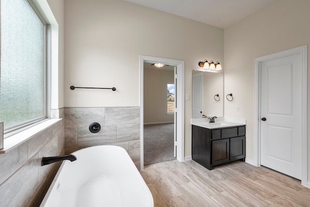 bathroom featuring wood-type flooring, a bath, a wealth of natural light, and vanity