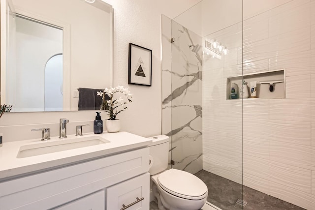 bathroom with toilet, vanity, and a tile shower