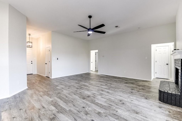 unfurnished living room featuring light hardwood / wood-style floors, ceiling fan with notable chandelier, and a brick fireplace