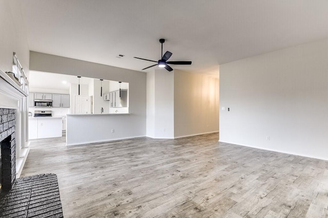 unfurnished living room with light wood-type flooring, ceiling fan, and a fireplace