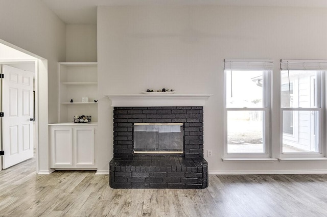 unfurnished living room featuring built in shelves, light hardwood / wood-style floors, and a fireplace