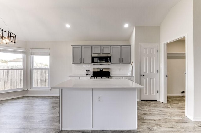 kitchen featuring pendant lighting, appliances with stainless steel finishes, backsplash, gray cabinets, and a center island