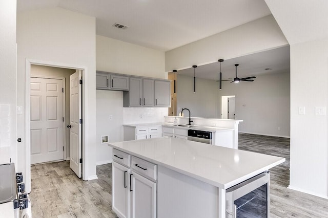 kitchen with gray cabinetry, sink, a kitchen island, light hardwood / wood-style flooring, and beverage cooler