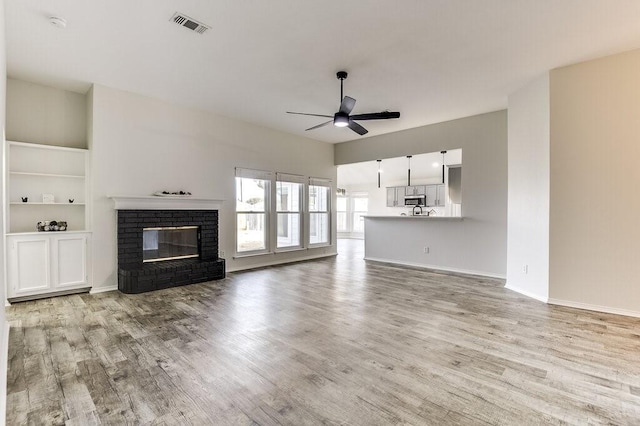 unfurnished living room featuring built in shelves, light hardwood / wood-style floors, a fireplace, and ceiling fan