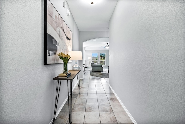 corridor with light tile patterned floors, a textured wall, arched walkways, and baseboards