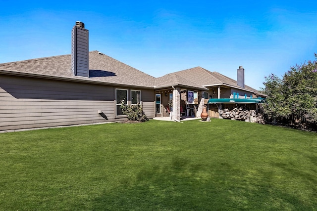 back of house featuring roof with shingles, a lawn, and a chimney