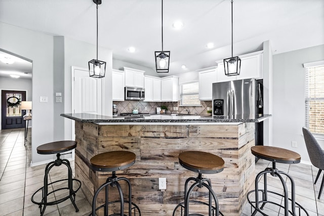 kitchen with appliances with stainless steel finishes, a kitchen island, white cabinets, a kitchen bar, and decorative light fixtures