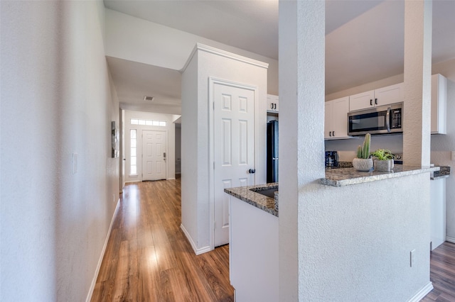 kitchen featuring black refrigerator, white cabinetry, light hardwood / wood-style flooring, and stone counters