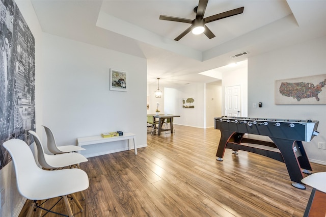 rec room with ceiling fan, hardwood / wood-style floors, and a tray ceiling