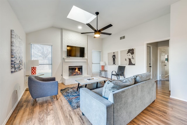 living room featuring ceiling fan, vaulted ceiling with skylight, hardwood / wood-style floors, and a fireplace