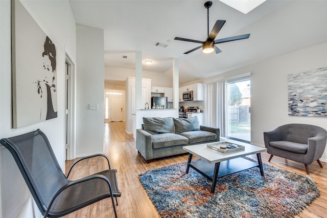 living room with a skylight, light hardwood / wood-style floors, and ceiling fan