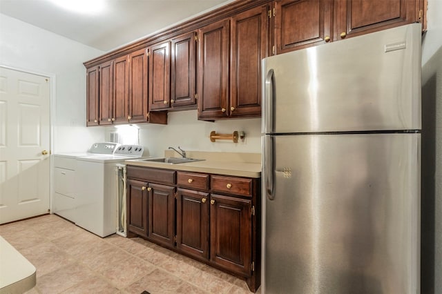 kitchen featuring sink, washing machine and clothes dryer, light tile patterned floors, and stainless steel fridge