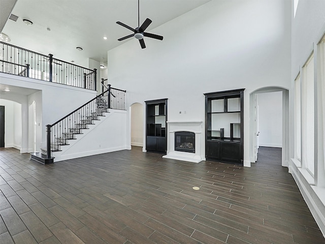 unfurnished living room with dark wood-type flooring, ceiling fan, and a high ceiling