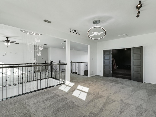 spare room with carpet flooring, ceiling fan with notable chandelier, and rail lighting