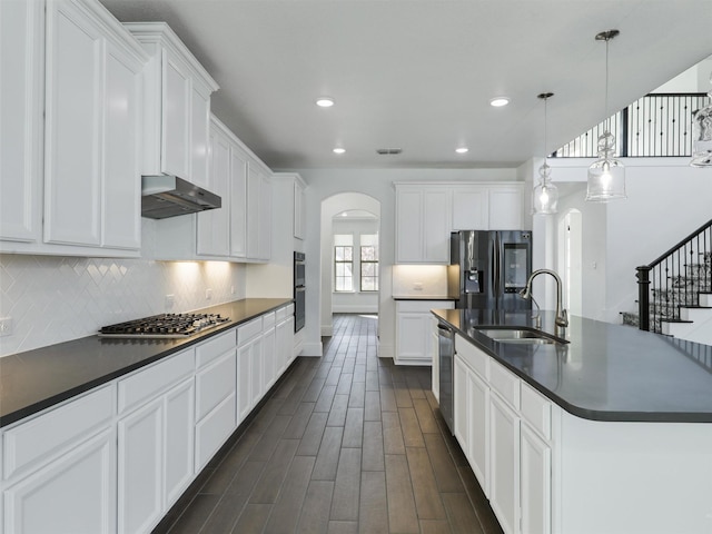 kitchen featuring stainless steel appliances, an island with sink, white cabinetry, and decorative light fixtures