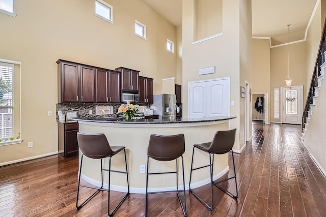 kitchen with backsplash, a towering ceiling, dark brown cabinets, and stainless steel appliances