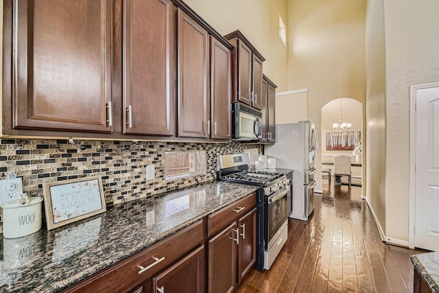 kitchen featuring stainless steel gas stove, a towering ceiling, dark stone counters, and decorative backsplash