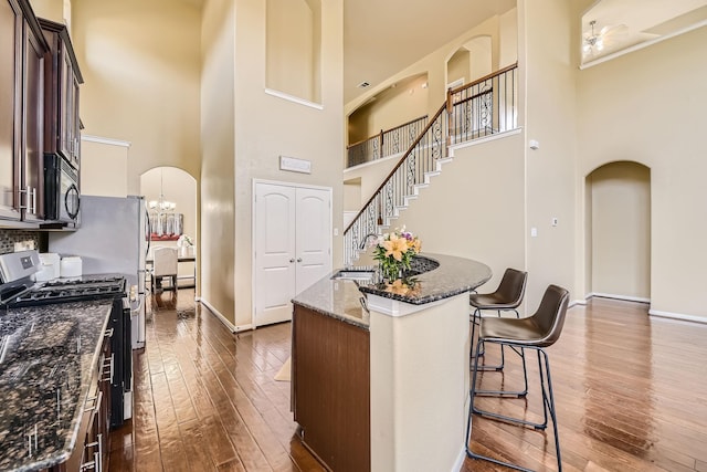 kitchen with a high ceiling, stainless steel gas range oven, an island with sink, and dark stone counters