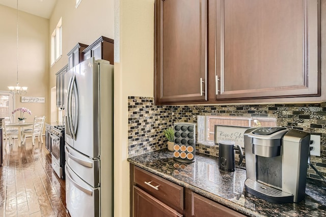 kitchen with appliances with stainless steel finishes, decorative light fixtures, dark stone counters, hardwood / wood-style flooring, and a notable chandelier