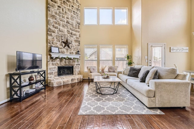 living room featuring a stone fireplace, dark wood-type flooring, and plenty of natural light