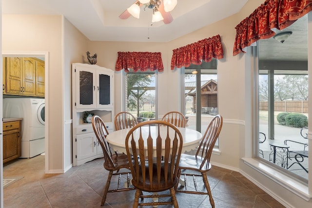 dining space featuring ceiling fan, washer / dryer, light tile patterned floors, and a tray ceiling