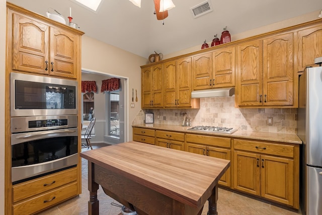 kitchen featuring butcher block counters, decorative backsplash, stainless steel appliances, and ceiling fan