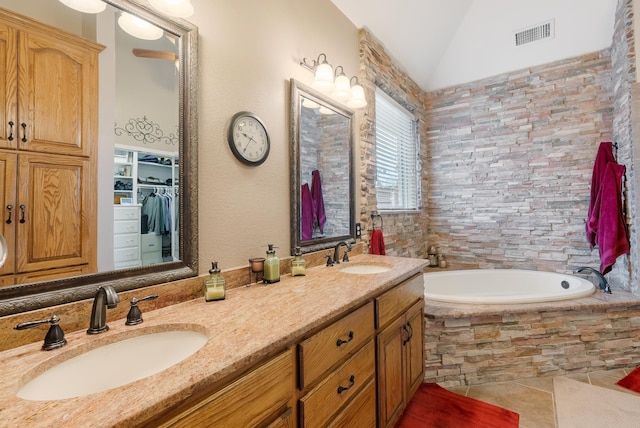 bathroom with lofted ceiling, tiled bath, and vanity