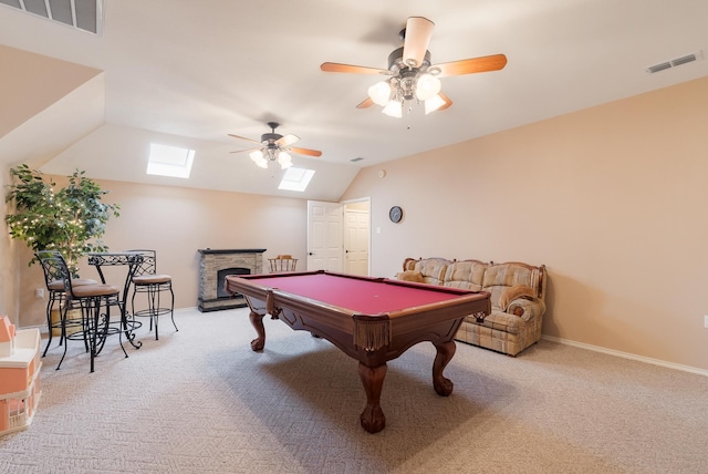 playroom with ceiling fan, light colored carpet, a fireplace, and vaulted ceiling with skylight