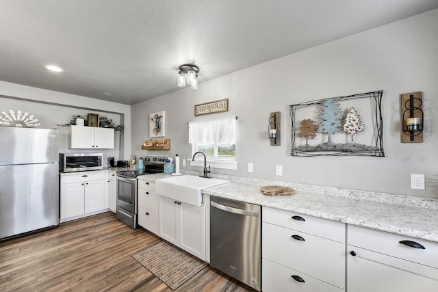 kitchen with sink, white cabinetry, light stone counters, dark hardwood / wood-style floors, and stainless steel appliances