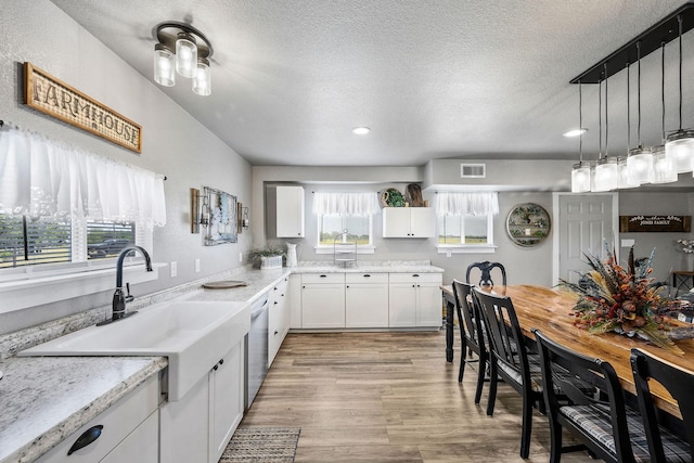 kitchen featuring light stone countertops, a textured ceiling, dishwasher, white cabinetry, and sink