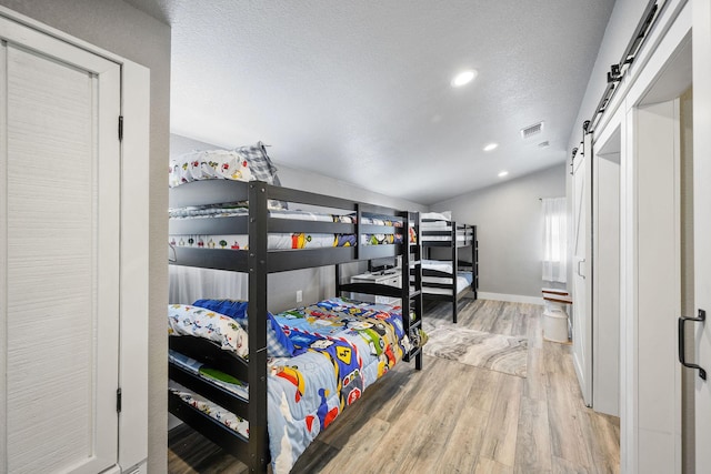 bedroom featuring light wood-type flooring, vaulted ceiling, a barn door, and a textured ceiling