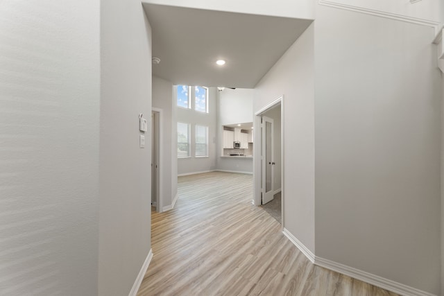 hallway with light hardwood / wood-style flooring and a towering ceiling