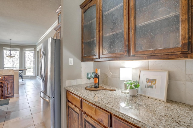 kitchen featuring crown molding, light tile patterned floors, stainless steel refrigerator, pendant lighting, and light stone countertops