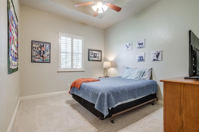 bedroom with light carpet, a tray ceiling, and ceiling fan