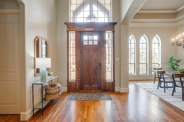 entrance foyer with ornamental molding, a healthy amount of sunlight, an inviting chandelier, and light hardwood / wood-style flooring