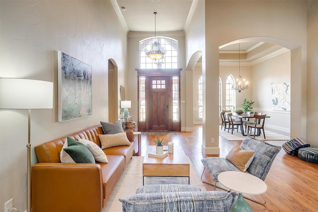 living room featuring crown molding, a towering ceiling, an inviting chandelier, and light hardwood / wood-style flooring