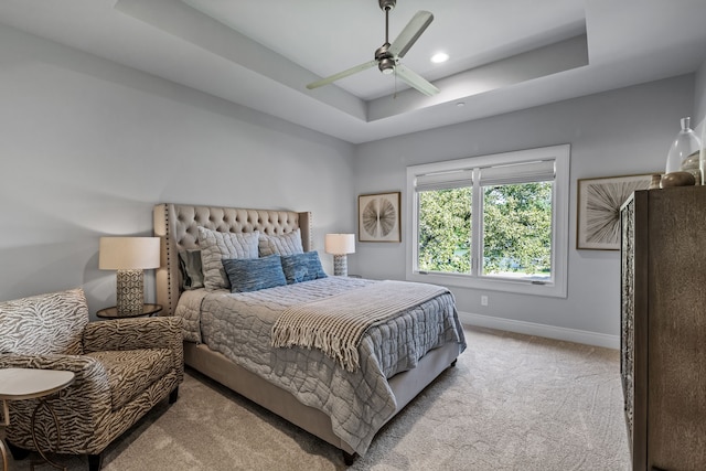 bedroom featuring ceiling fan, a tray ceiling, and light carpet