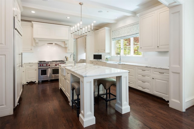 kitchen featuring light stone countertops, decorative light fixtures, an island with sink, double oven range, and sink