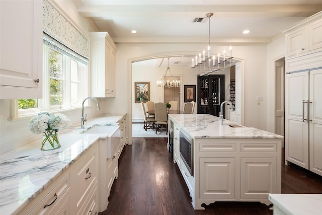 kitchen featuring white cabinets, an island with sink, hanging light fixtures, and light stone countertops