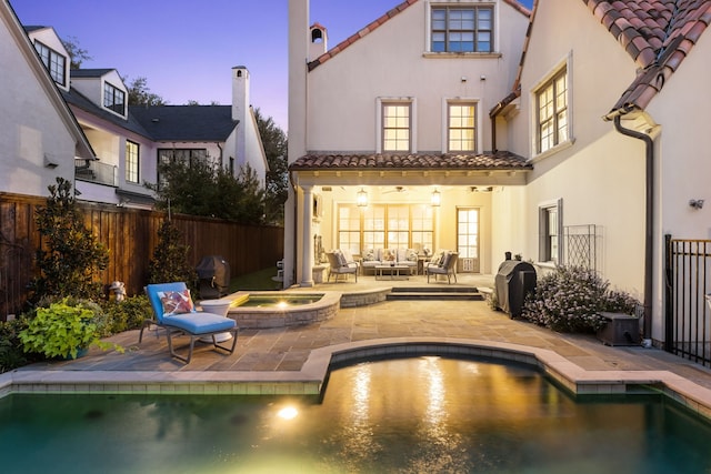 back house at dusk featuring a pool with hot tub, a patio area, and an outdoor hangout area