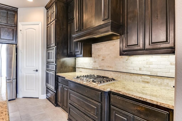 kitchen featuring light tile patterned flooring, dark brown cabinets, light stone countertops, and appliances with stainless steel finishes