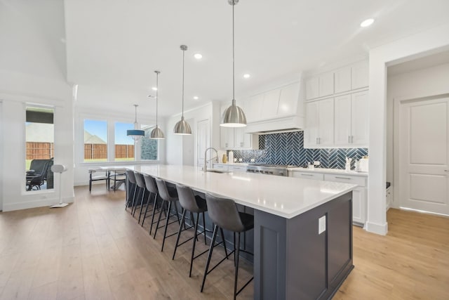 kitchen with decorative light fixtures, sink, white cabinetry, a large island with sink, and a breakfast bar area