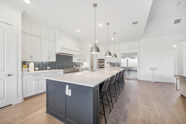 kitchen featuring visible vents, stainless steel appliances, premium range hood, white cabinetry, and a sink