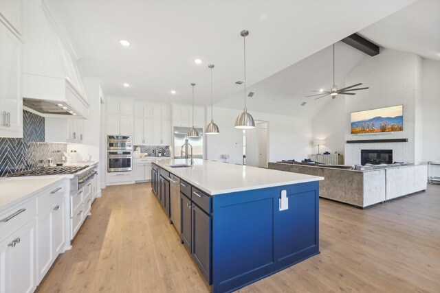 kitchen with a large island with sink, white cabinets, appliances with stainless steel finishes, premium range hood, and hanging light fixtures