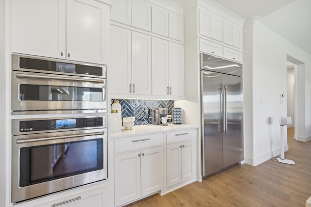 kitchen with white cabinets, appliances with stainless steel finishes, light countertops, light wood-type flooring, and backsplash