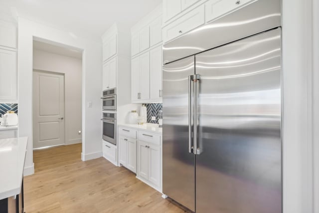 kitchen featuring light wood-style flooring, white cabinetry, light countertops, appliances with stainless steel finishes, and decorative backsplash