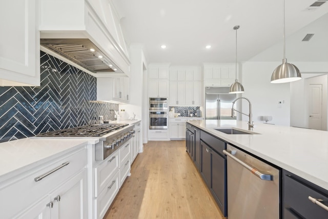 kitchen with light countertops, visible vents, appliances with stainless steel finishes, a sink, and premium range hood