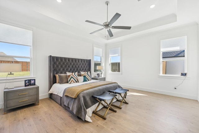 bedroom featuring a tray ceiling, multiple windows, light wood-style flooring, and baseboards